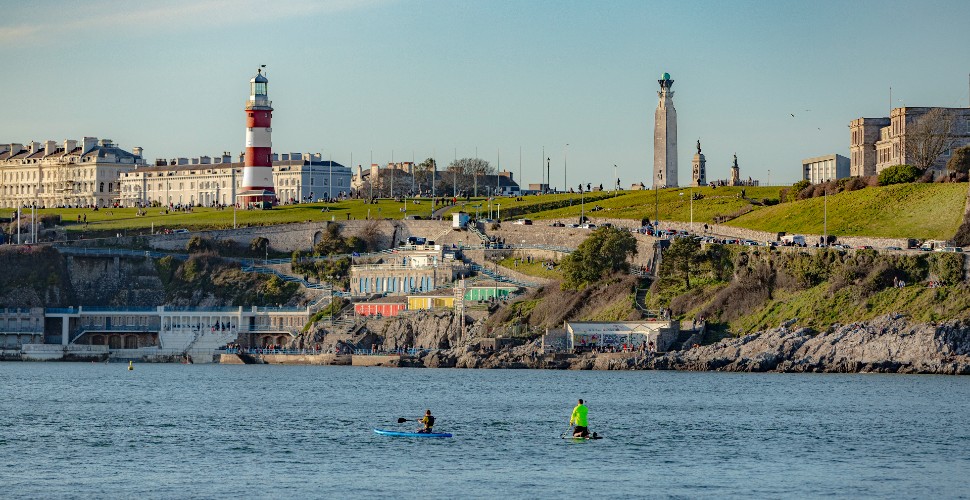 Two people paddle boarding in Plymouth Sound with Plymouth Hoe in the background